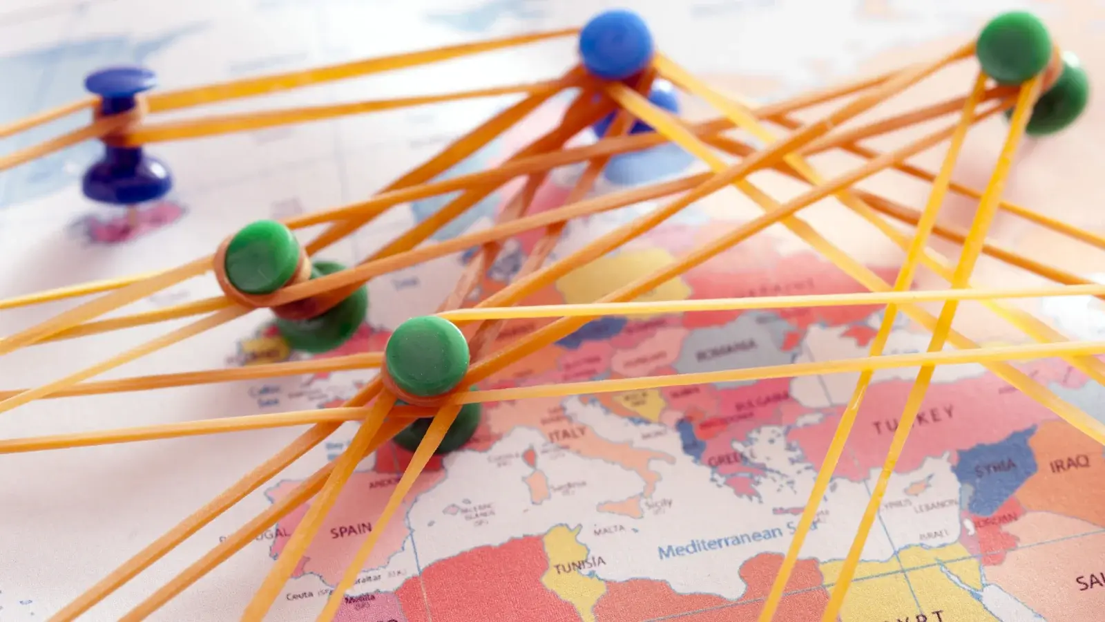 Vários alfinetes coloridos ligados por elástico espetados em um mapa mundi.